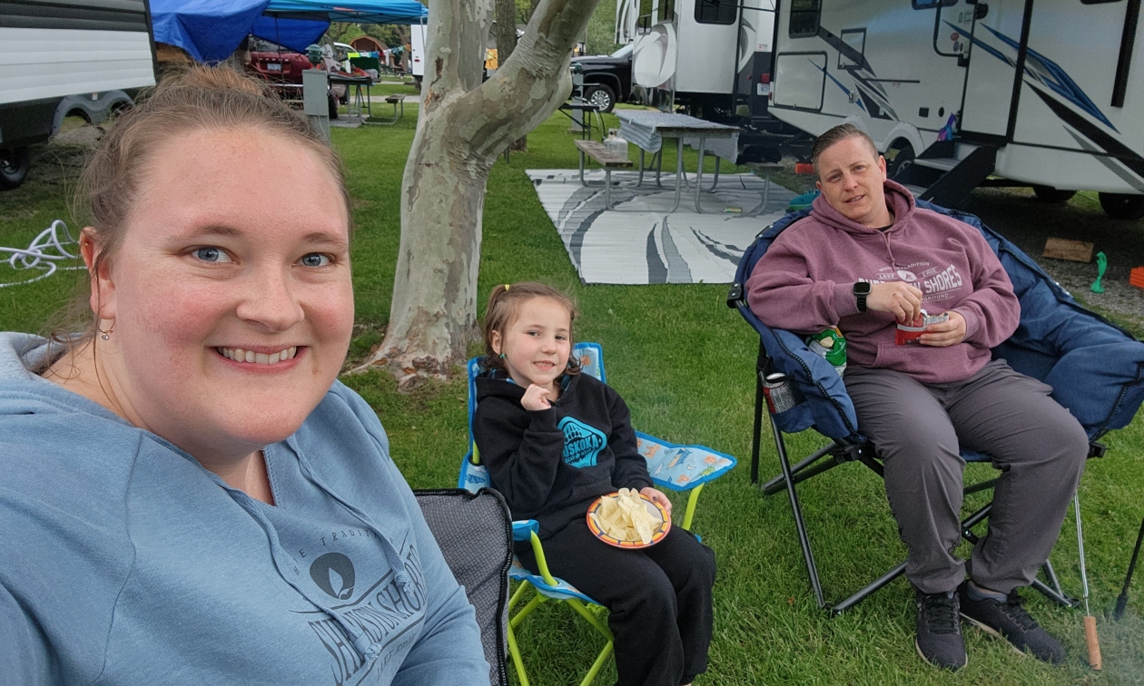 Two women and a child sitting around a campsite