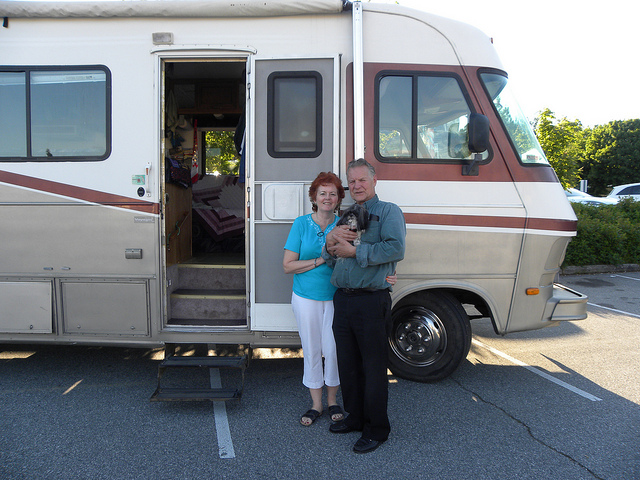 Barb and Dave Rees standing outside their rig with their little dog. 