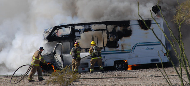 An RV on fire with a number of firefighters trying to put out the flames. 