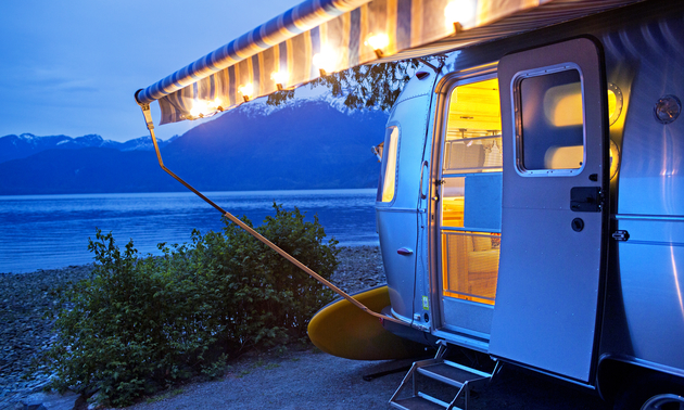 Boler-style RV parked at night with an awning pulled out and lights around it