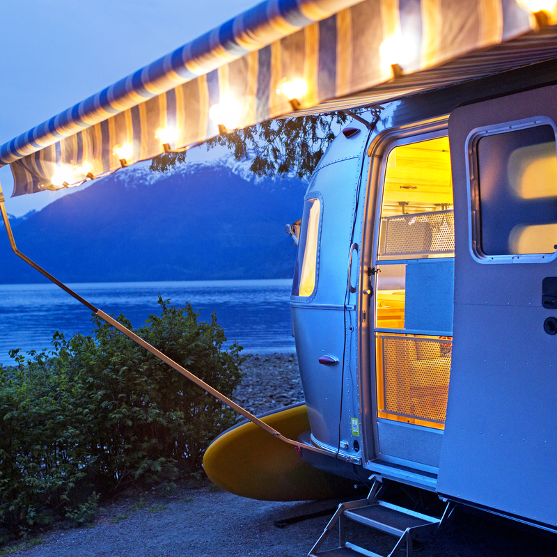 Boler-style RV parked at night with an awning pulled out and lights around it