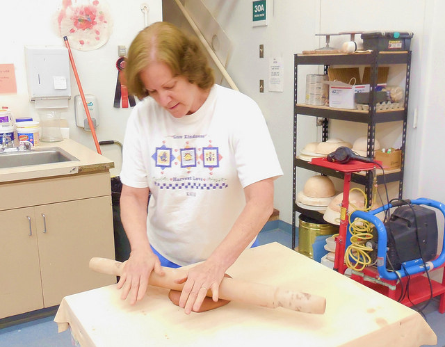 Pottery studio manager Kathleen Birkholz rolling out a piece of pottery with a rolling pin.