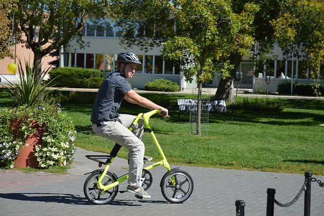 A young man riding a bright yellow Strida bike