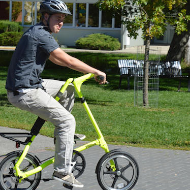 A young man riding a bright yellow Strida bike