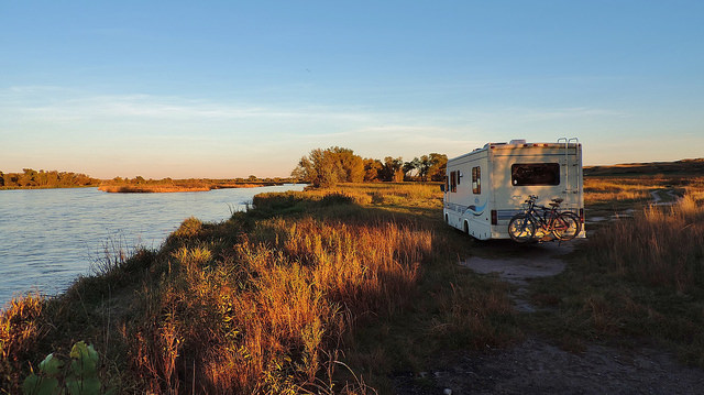 A photo of Sherman, the Read's motorhome next to a grassy river bank at sunset.