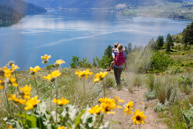 A mother who is carrying her child piggy-back style is walking down the trail at the Kalamalka Lake Provincial Park.