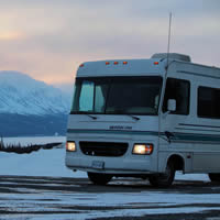 An RV on snowy road with snowy mountains in the background. 