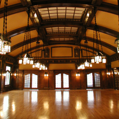 The Royal Alexandra Hall has a high, arched roof with wooden beams stretching across its ceiling. Bright, exquisite chandeliers hang low from up above.