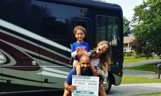 Family of three - mom, dad and child, in front of a Class A RV