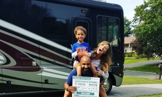 Family of three - mom, dad and child, in front of a Class A RV