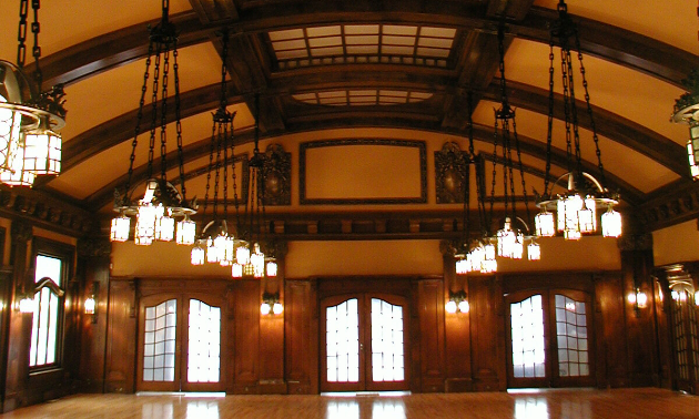 The Royal Alexandra Hall has a high, arched roof with wooden beams stretching across its ceiling. Bright, exquisite chandeliers hang low from up above.