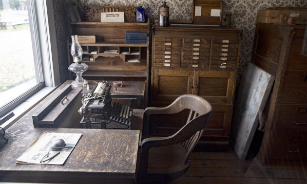 A typewriter sits on an old, worn brown desk next to old cabinets in an office.