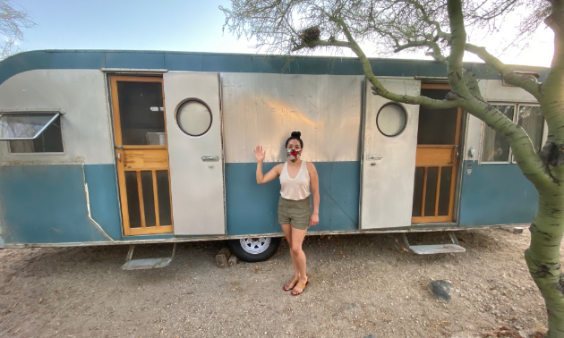 Stephanie Loya stands in front of her blue and white 1953 28-foot Platt Trail-a-Home travel trailer. 