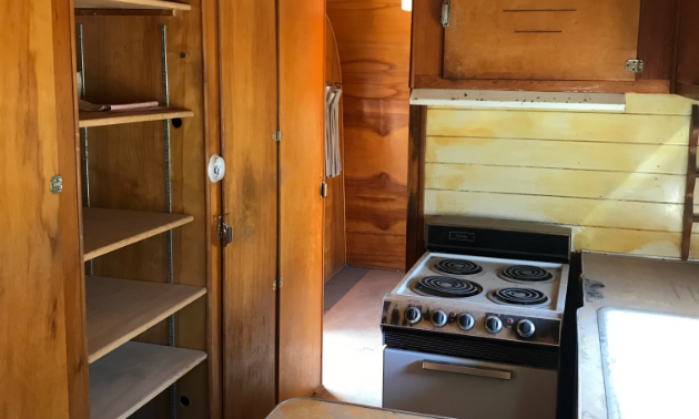 The interior of the 1953 28-foot Platt Trail-a-Home travel trailer has wooden cupboards and a miniature stove.