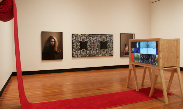 A red piece of cloth is draped off the wall onto part of the floor. A cabinet is propped up in the middle of the room. A mesmerizing portrait separates two odd photos.