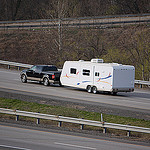 A picture of a pickup truck pulling a long white RV trailer on a highway. 