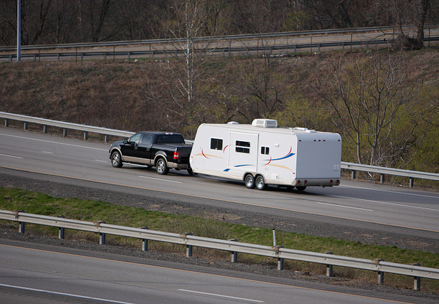 A picture of a pickup truck pulling a long white RV trailer on a highway. 