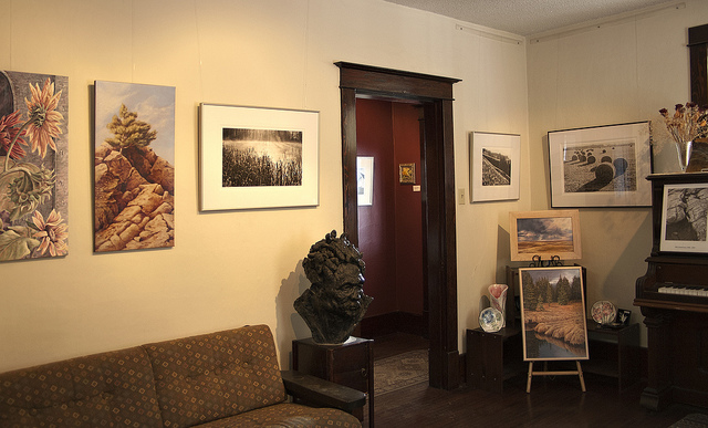 This picture shows the inside of the gallery, with a couple of flower paintings, as well as 4 black and white prairie scene photographs. 