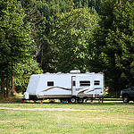 Picture of a  white RV trailer parked in a field with some trees behind it.