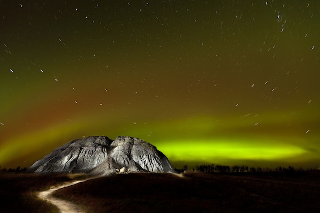Northern lights in greens and yellows against a mountain.