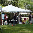 A white tent displays a number of art works and is surrounded by people and green lawn.