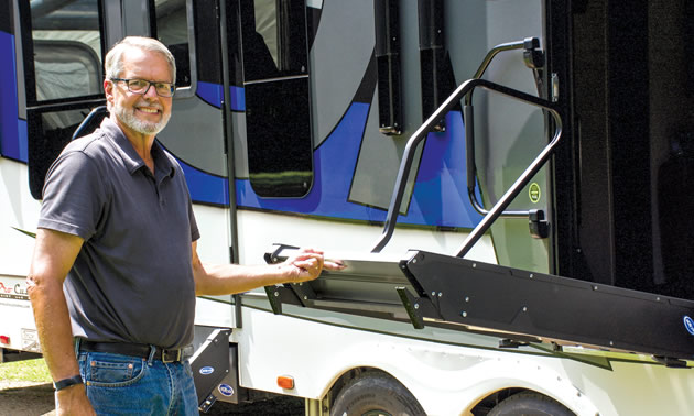 Man standing beside RV and showing how stairs fold up. 