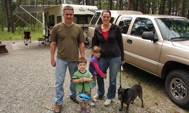 Couple with two small children and a small dog stand in their campsite.