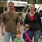 Couple with two small children and a small dog stand in their campsite.