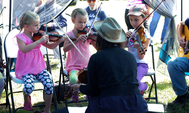 Three young girls playing fiddles, along with adult playing fiddle.
