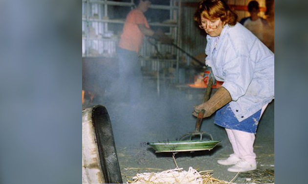 a woman using a large pitchfork to put a piece of raku pottery into a bed of straw to cool after being fired