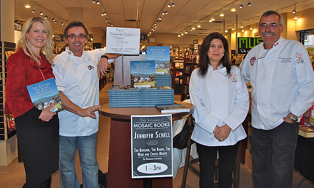 Woman in red, holding a book, stands with two men and a woman in chefs' wear, with a notice about a book signing.