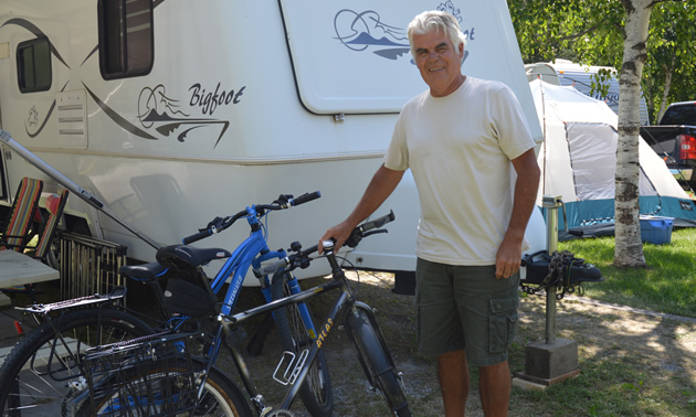 Fit-looking senior man with two bicycles and a travel trailer in the background