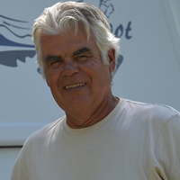 Fit-looking senior man with two bicycles and a travel trailer in the background