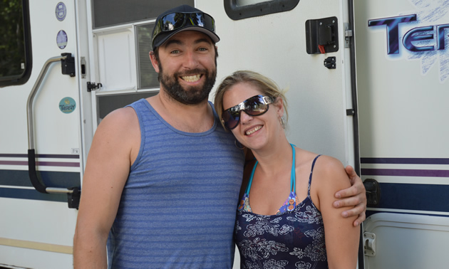 Young couple in summer clothing stand outside a large RV unit