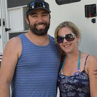 Young couple in summer clothing stand outside a large RV unit