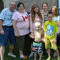 Two adults and five children outside an open tent-trailer