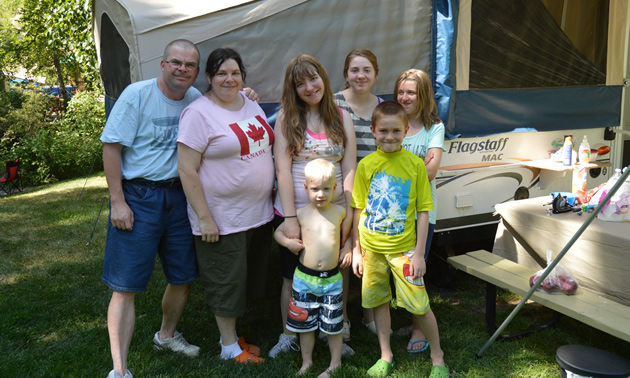 Two adults and five children outside an open tent-trailer