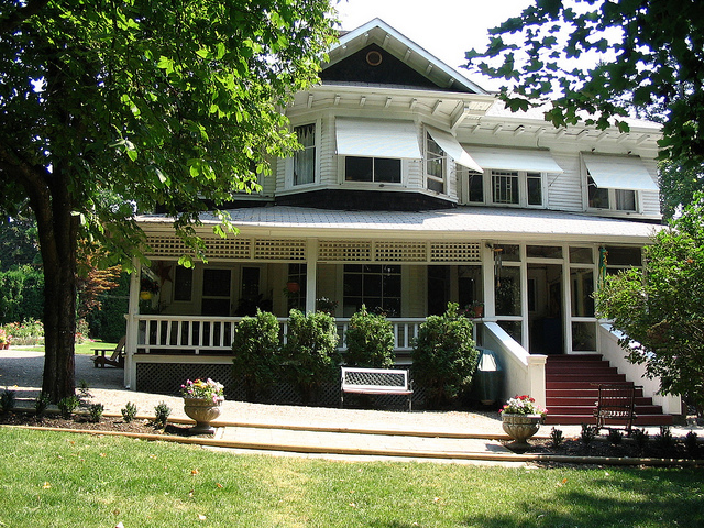 Photo of a beautiful historic house with a large white front porch, awnings and gable windows. 