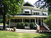 Photo of a beautiful historic house with a large white front porch, awnings and gable windows. 