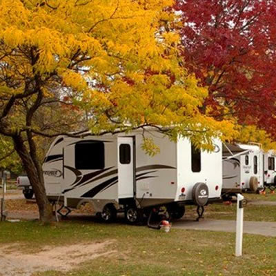 A row of campers in an RV park, with colourful red and yellow autumn trees lining the RV lots. 