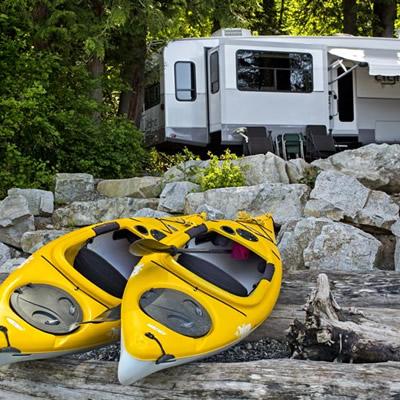 Two yellow kayaks sitting on beach, with camper parked in background. 