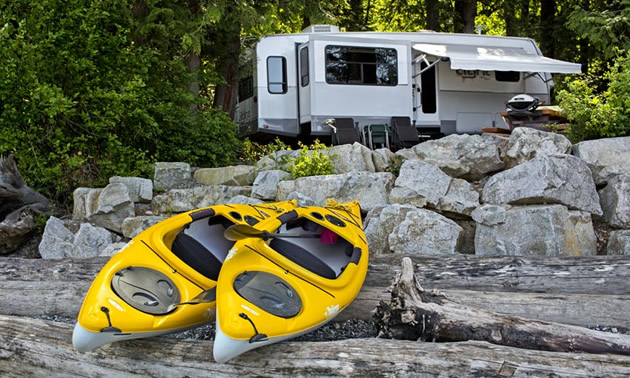 Two yellow kayaks sitting on beach, with camper parked in background. 