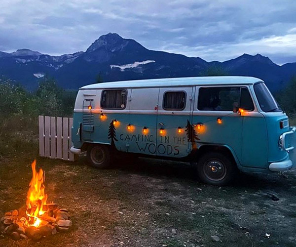 Blue and white VW van with picket fence and campfire. 