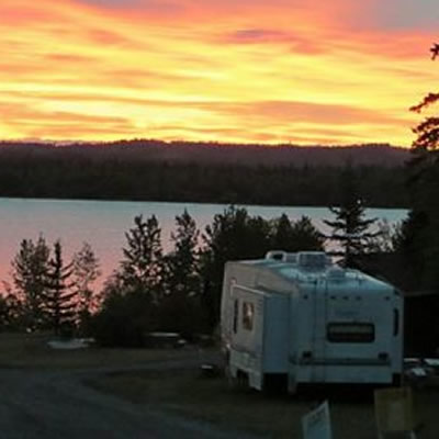 Camper parked in spot overlooking lake as sun sets. 