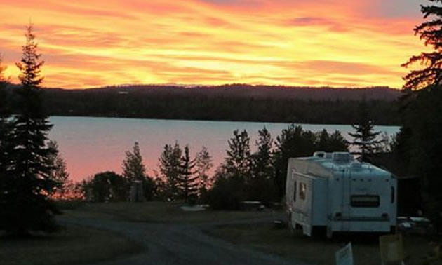 Camper parked in spot overlooking lake as sun sets. 