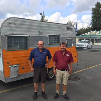 The two sons of Kustom Koach founder Carl Carstensen standing in front of trailer. 