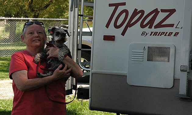 Woman holding small dog stands beside her RV unit.