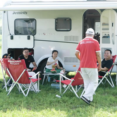 Group of people sitting outside in front of motorhome. 