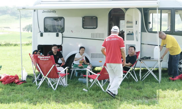Group of people sitting outside in front of motorhome. 