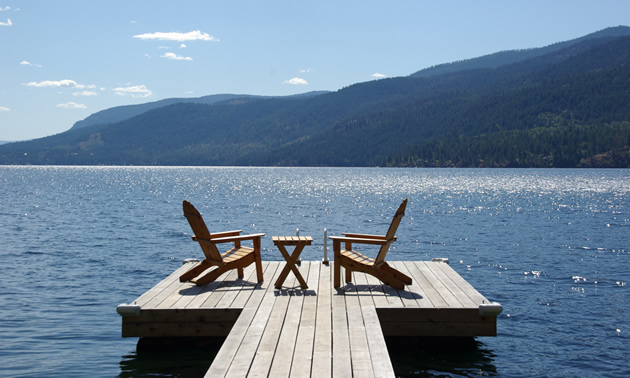 Two lounge chairs await on a dock extending over Christina Lake, B.C.